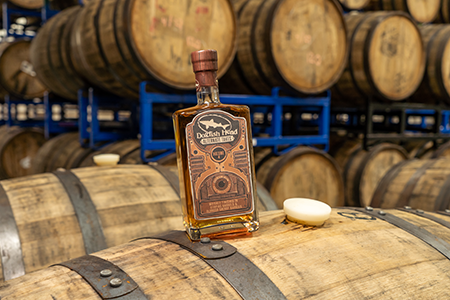 A bottle Alternate Takes IV sitting ontop of aging whiskey barrels.