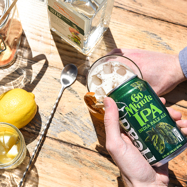 Birds eye view shot of someone pouring a 60 Minute IPA into a cocktail glass surrounded by cocktail ingredients