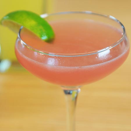 Glass filled with pink colored cocktail garnished with a lime slice