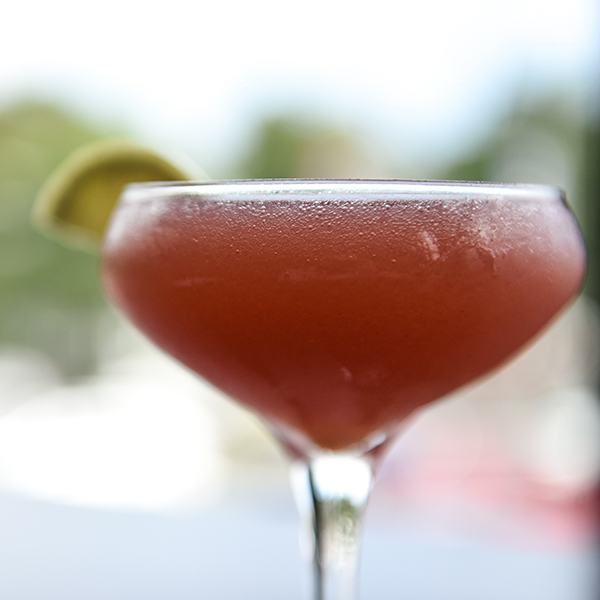 A glass filled with red cocktail garnished with a lime slice