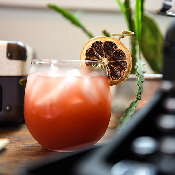 Cocktail in a glass garnished with a dried blood orange with a green plant in the background