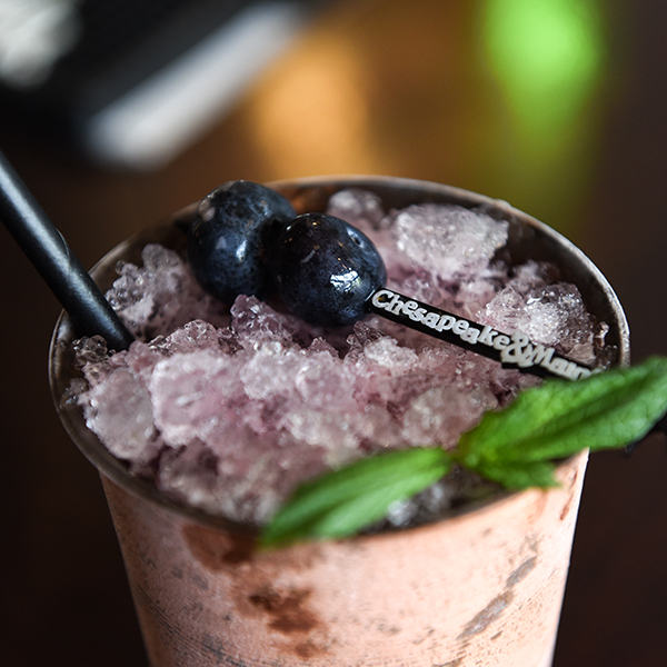 A glass filled with ice, blueberries, a straw, and mint leaves