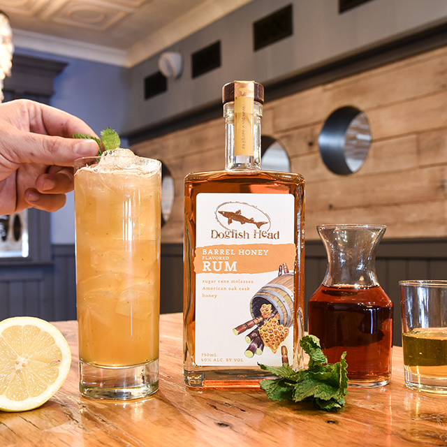 Rum Mint Tea cocktail being garnished with a sprig of mint with a bottle of Barrel Honey Rum sitting next to it