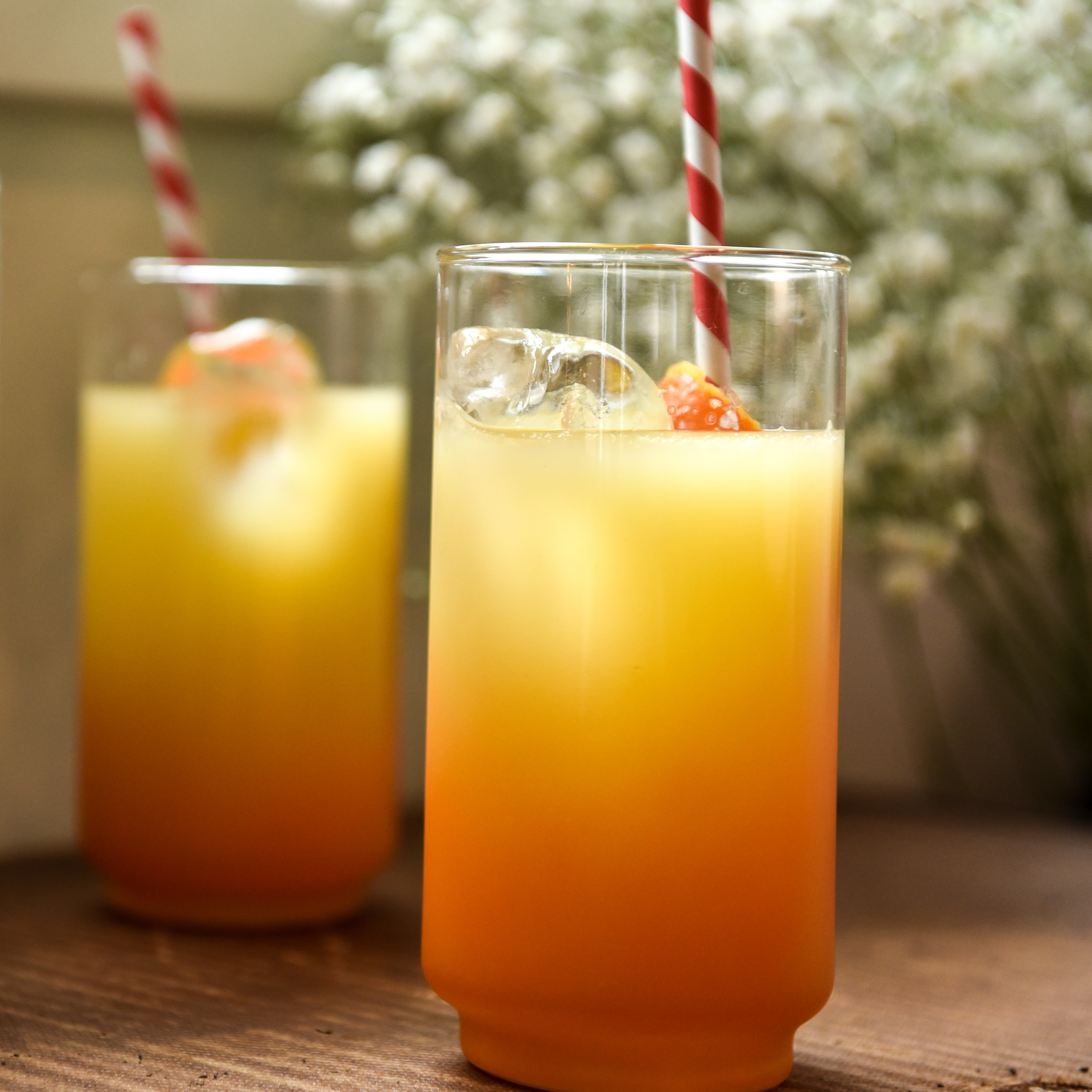 Glass with orange cocktail that has a red and white straw in it and there are two of these like it is in a mirror