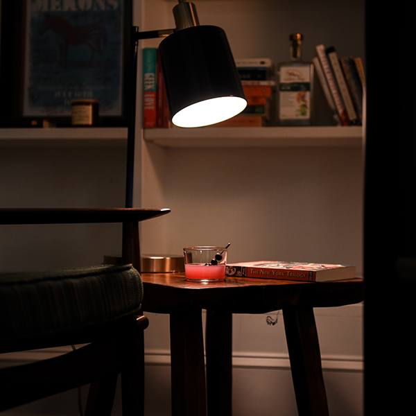 Compelling Blueberry Gimlet in a glass on a work desk in a dark room that is highlighted by a desk lamp