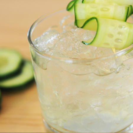 Drink on a table being garnished with cucumber slices