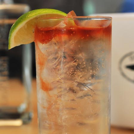 Glass on a table filled with cocktail garnished with a lime slice 