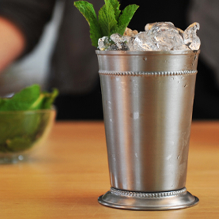 Silver cocktail shaker cup on a table that is garnished with mint 
