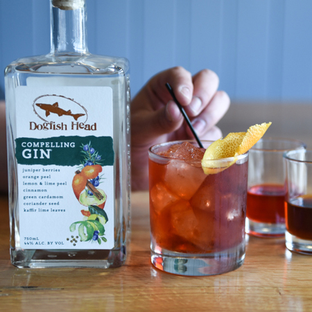 Compelling Gin bottle next to glass filled with Negroni cocktail and person's hand holding straw in the cocktail