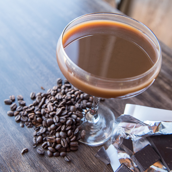 An espresso martini in a martini glass surrounded by coffee beans 