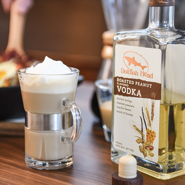 A bottle of Roasted Peanut Vodka next to a glass with cocktail topped with whipped cream