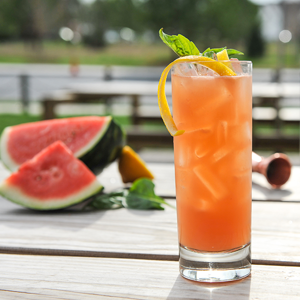 Watermelon Basil Smash Cocktail in a glass garnished with basil and lemon peel on a table with ingredients on the side