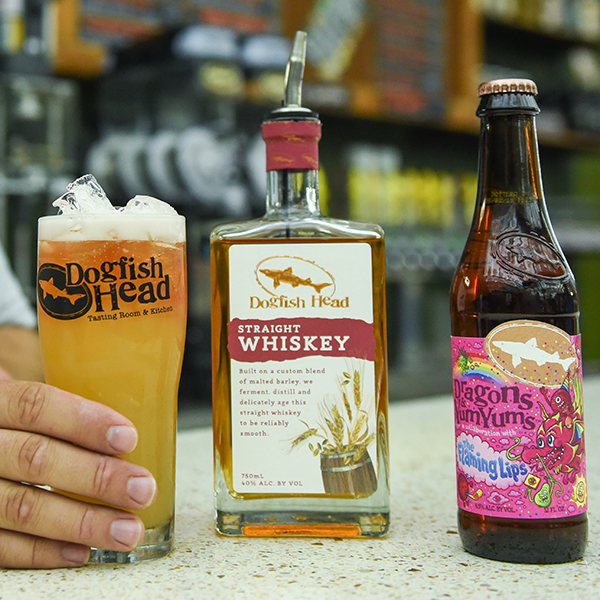 On the left, a Dogfish head glass filled with cocktail, in the middle a bottle of Straight Whiskey, and on the right a bottle of Dragons & YumYums