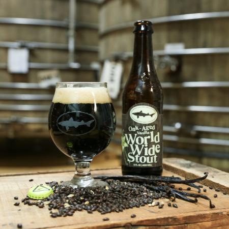 photo of a 16 oz bottle of stout beer with a distillery and wooden barrels in the background