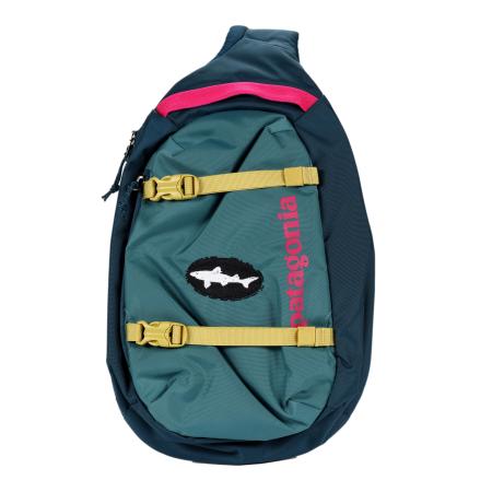 Front view of a Patagonia sling backpack in teal and navy with bright yellow buckle straps, a hot pink accent, and a black oval patch featuring the white Dogfish Head shark logo. “Patagonia” is printed vertically in pink along the front.