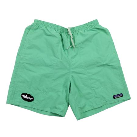 Front view of light green Patagonia shorts featuring a white drawstring waist, a black Dogfish Head shark logo patch on the left leg, and a classic Patagonia logo tag on the right leg.