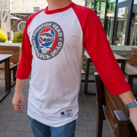 Person wearing a white and red raglan-style baseball tee featuring a circular Dogfish Head x Grateful Dead graphic on the chest.