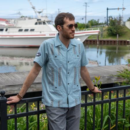 Male model wearing Howler button down short sleeve shirt with multi colored embroidery and two Dogfish Head embroidered logos on each sleeve. 