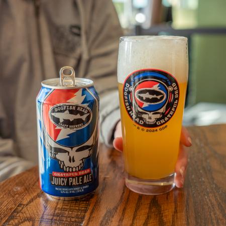 A pint glass with the Dogfish Head x Grateful Dead collaboration logo on the front. Pictured here being filled up with beer next to the collaboration beer can.