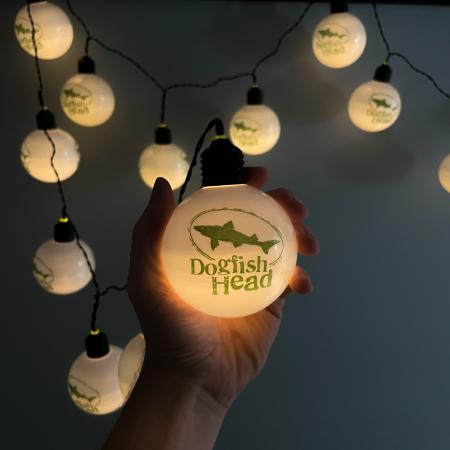 Dogfish Head Round String Lights Lit Up In The Dark Being Held By a Model To Show Size