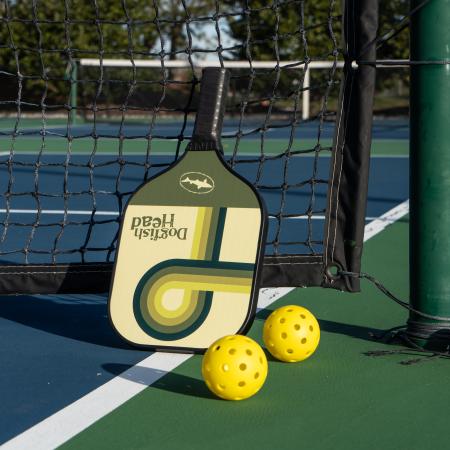 Dogfish Head Pickle Ball Paddle in a Green and White Retro Design On a Pickle Ball Court