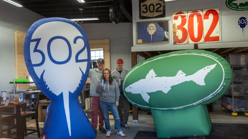 On the left, a giant blue inflatable with the 302 Horseshoe Crab logo. On the right, a giant green inflatable with the 302 Dogfish Head logo. 3 people standing in the middle. 