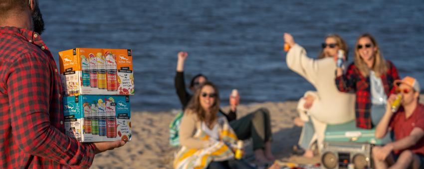 Group of friends having fun on the beach with Dogfish Head canned cocktails