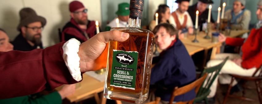 Scull & Crossbones Apertif bottle being held by hand in front of people sitting at table