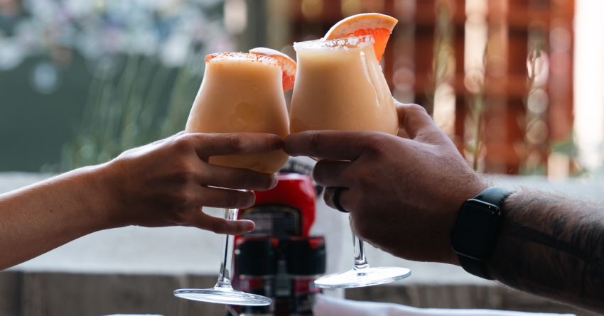 two wine glasses filled with a peach colored shushy, held by 2 people cheers-ing