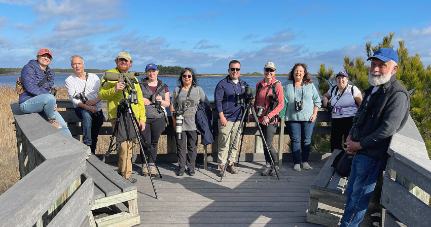 A photo of 10 adults lined up on a boardwalk with a body of water in the background