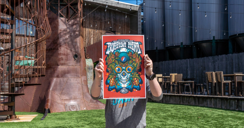 2025 Record Store Day poster being held up by a person with a brewery behind them