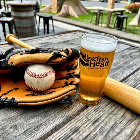 baseball, mitt, and glove on a table with a pint glass full of beer with the Dogfish Head logo on it