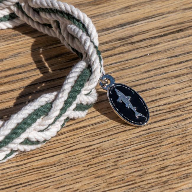 Dogfish Head Rope Bracelet with Charm photographed on a wood surface. Close up of charm detailing featuring the Shark & Shield logo 