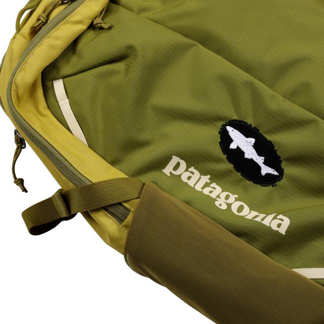 Close-up of the front pocket area on the backpack displaying the embroidered white “patagonia” text and the black Dogfish Head logo patch against the olive green fabric.