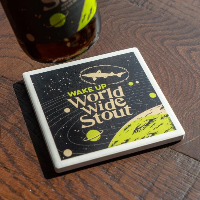 World Wide Stout Coaster With White and Green Galaxy On Black Background And Dogfish Head Shark Logo