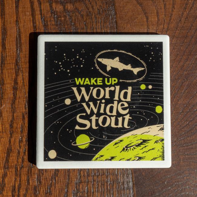 World Wide Stout Coaster With White and Green Galaxy On Black Background And Dogfish Head Shark Logo