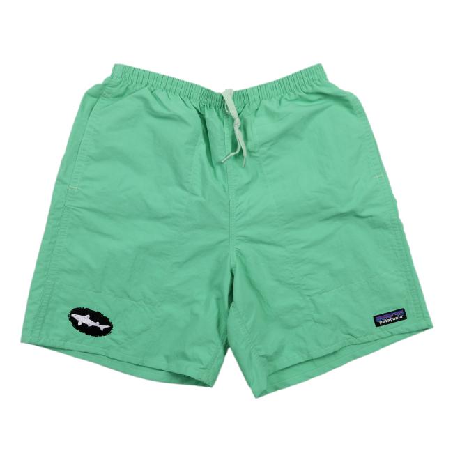 Front view of light green Patagonia shorts featuring a white drawstring waist, a black Dogfish Head shark logo patch on the left leg, and a classic Patagonia logo tag on the right leg.