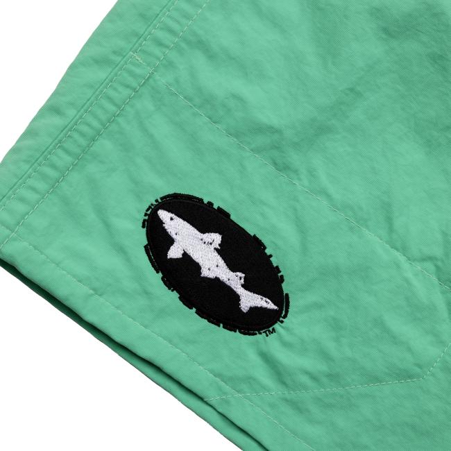 Close-up of the left leg of the green shorts showing the black oval Dogfish Head patch with a white embroidered shark logo.