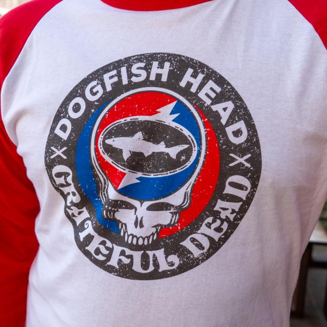 Close-up of the front graphic on the baseball tee, showing a circular logo with the Dogfish Head shark inside a red, white, and blue skull motif surrounded by the text “DOGFISH HEAD x GRATEFUL DEAD.”