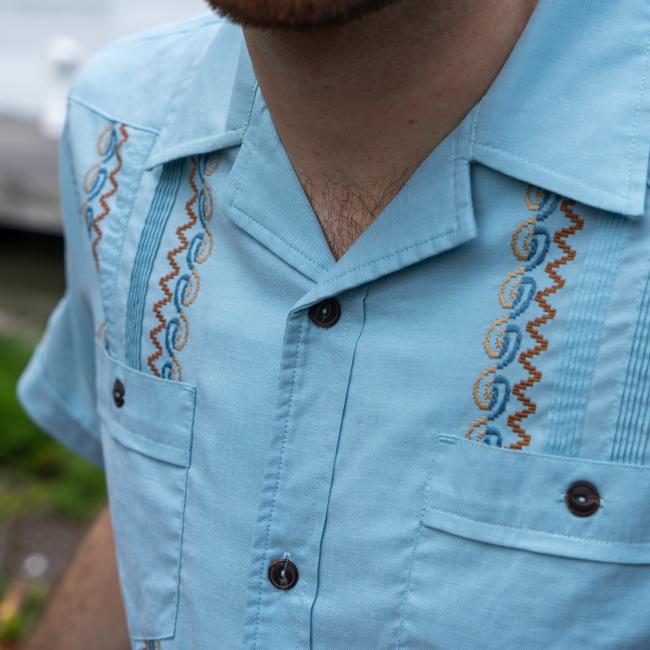 Close up of collar and front two pockets of blue button up shirt with multi color embroidery