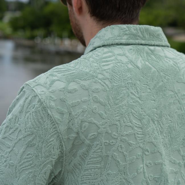Male model wearing Howler short sleeve textured terry polo. Close up shot of back of polo showing detailed texture of fabrication