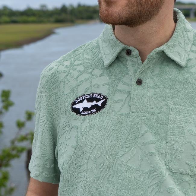 Male model wearing Howler short sleeve textured terry polo with Dogfish Head Since 95 embroidered logo. Close up of embroidered logo