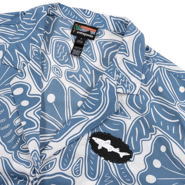 Close-up of the Patagonia shirt’s collar showing the fabric pattern details, Patagonia tag, and an embroidered black oval patch with the white Dogfish Head shark logo on the left chest.