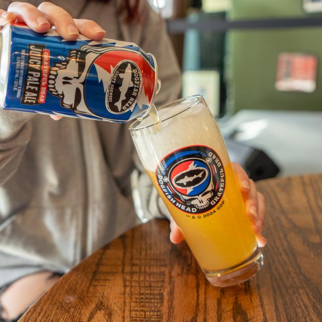 A pint glass with the Dogfish Head x Grateful Dead collaboration logo on the front. Pictured here being filled up with beer.