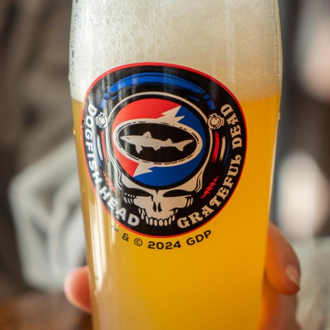 A pint glass with the Dogfish Head x Grateful Dead collaboration logo on the front. Close up pictured here filled with beer.