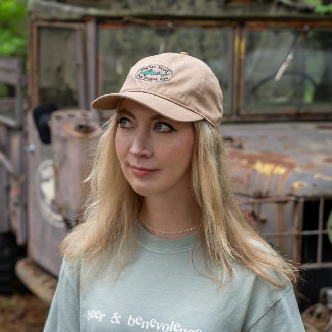 Person wearing a tan Dogfish Head hat with embroidered logo on the front, standing in front of a rustic, vintage truck.