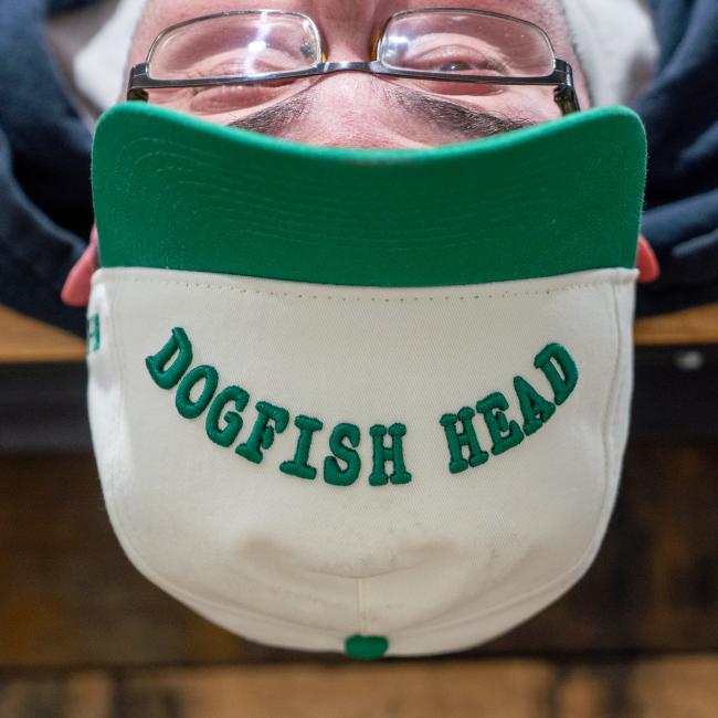 A cream colored five panel hat with a green brim and green embroidery that says 