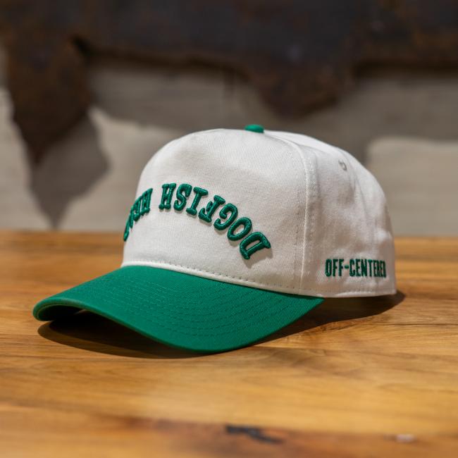 A cream colored five panel hat with a green brim and green embroidery that says 