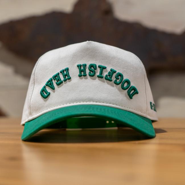 A cream colored five panel hat with a green brim and green embroidery that says 
