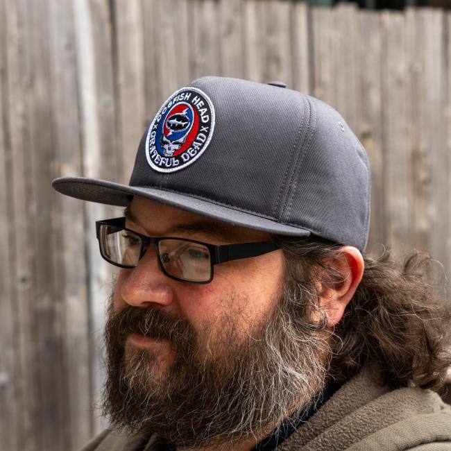 A charcoal colored flat brim hat with the Dogfish Head and Grateful Dead collaboration logo on the front.